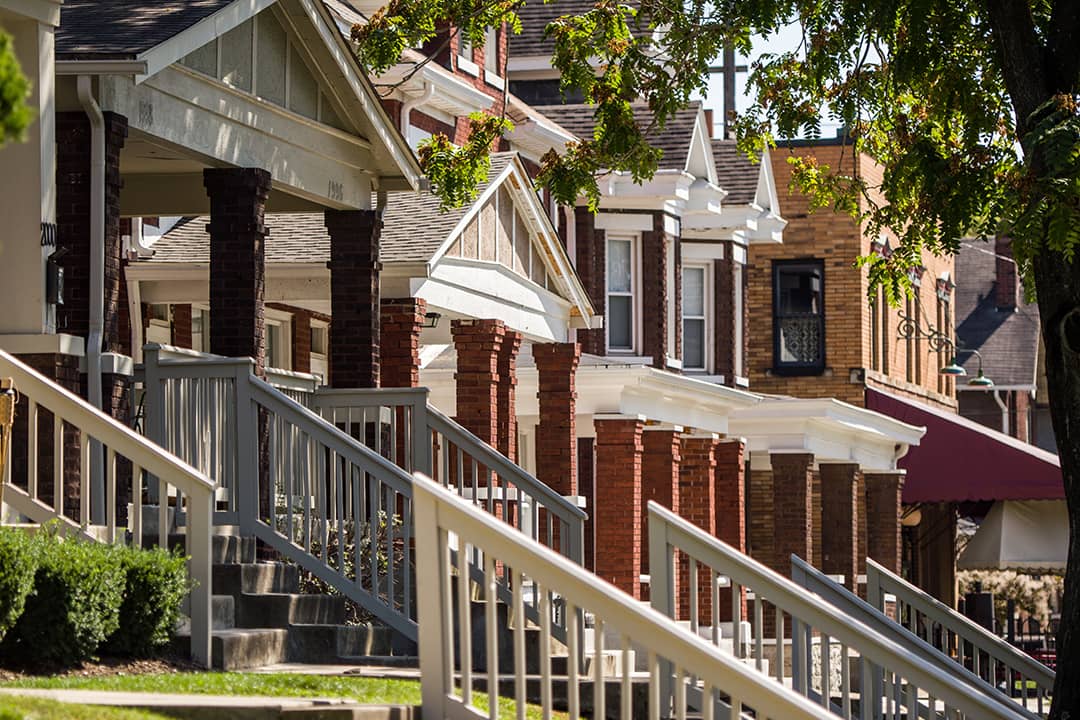 A row of American homes featuring front porches with brick columns and wooden railings.